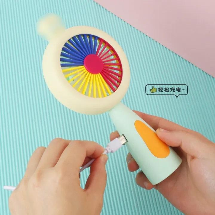Colorful toy with a light on top, held by a hand against a light pink background.